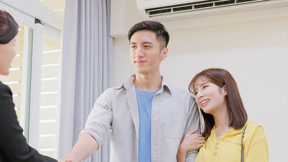 一對年輕情侶在看房時微笑與中介人交談，畫面呈現買房攻略中看屋諮詢的情景